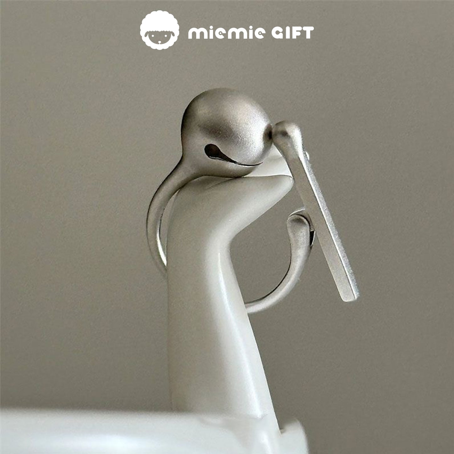 A side view of the Wooden Fish Silver Ring elegantly displayed on a ceramic holder, highlighting its smooth 925 sterling silver finish and functional wooden fish mallet design, perfect for stress relief and mindfulness, by MieMie Gift.